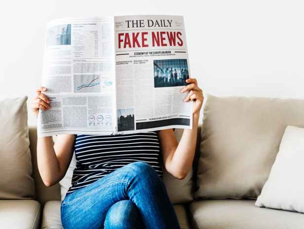 person reading the daily fake news newspaper sitting on gray couch